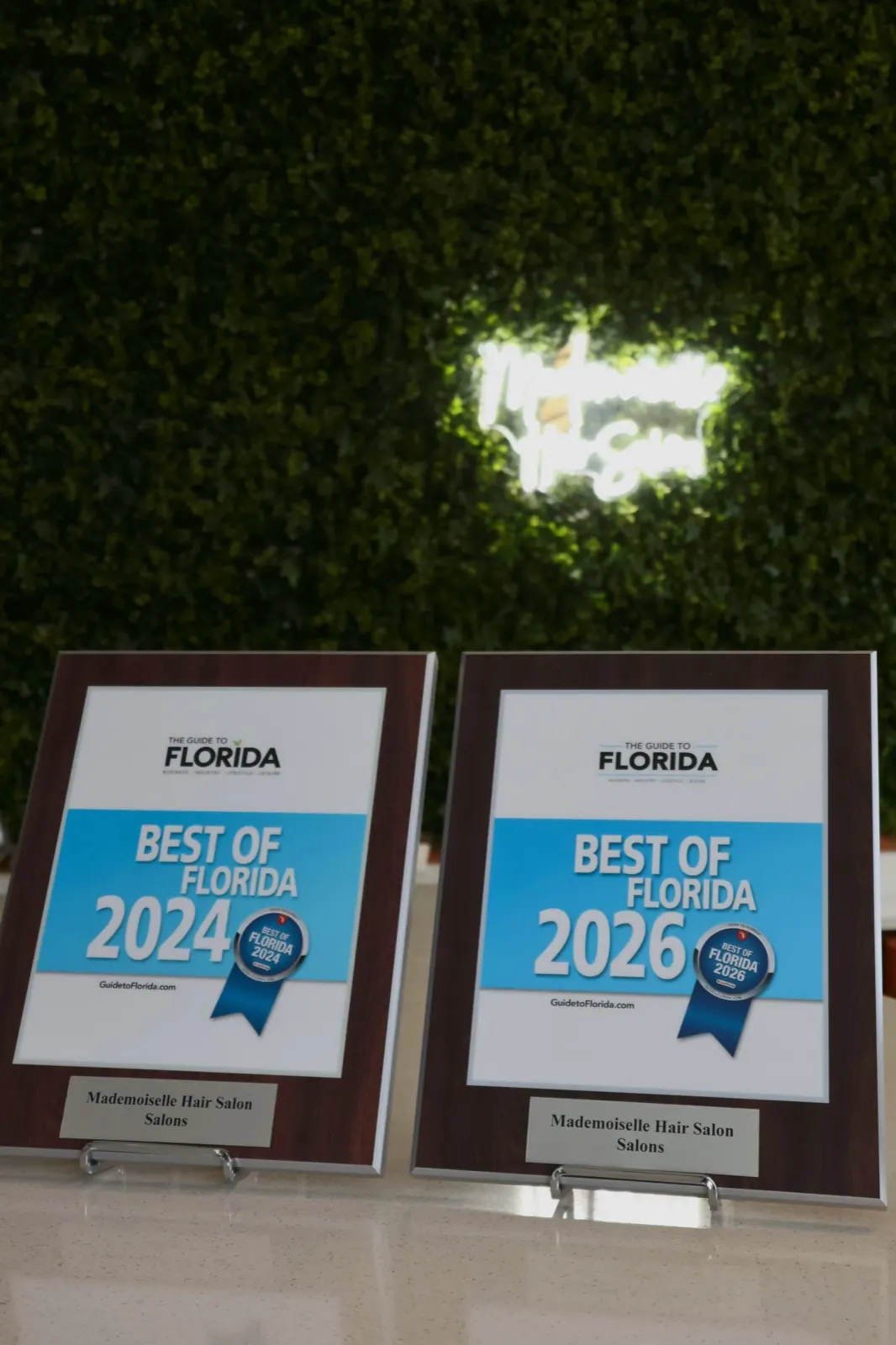 Best of Florida 2024 and 2026 plaques in front of the salon green wall